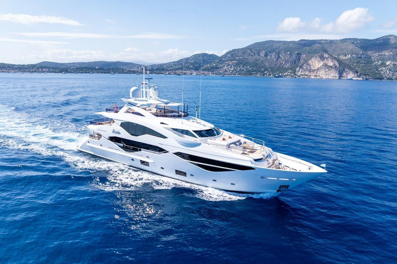 A sleek, modern yacht cruising on calm blue waters with a scenic coastline in the background. aboard ALADDIN Yacht for Sale