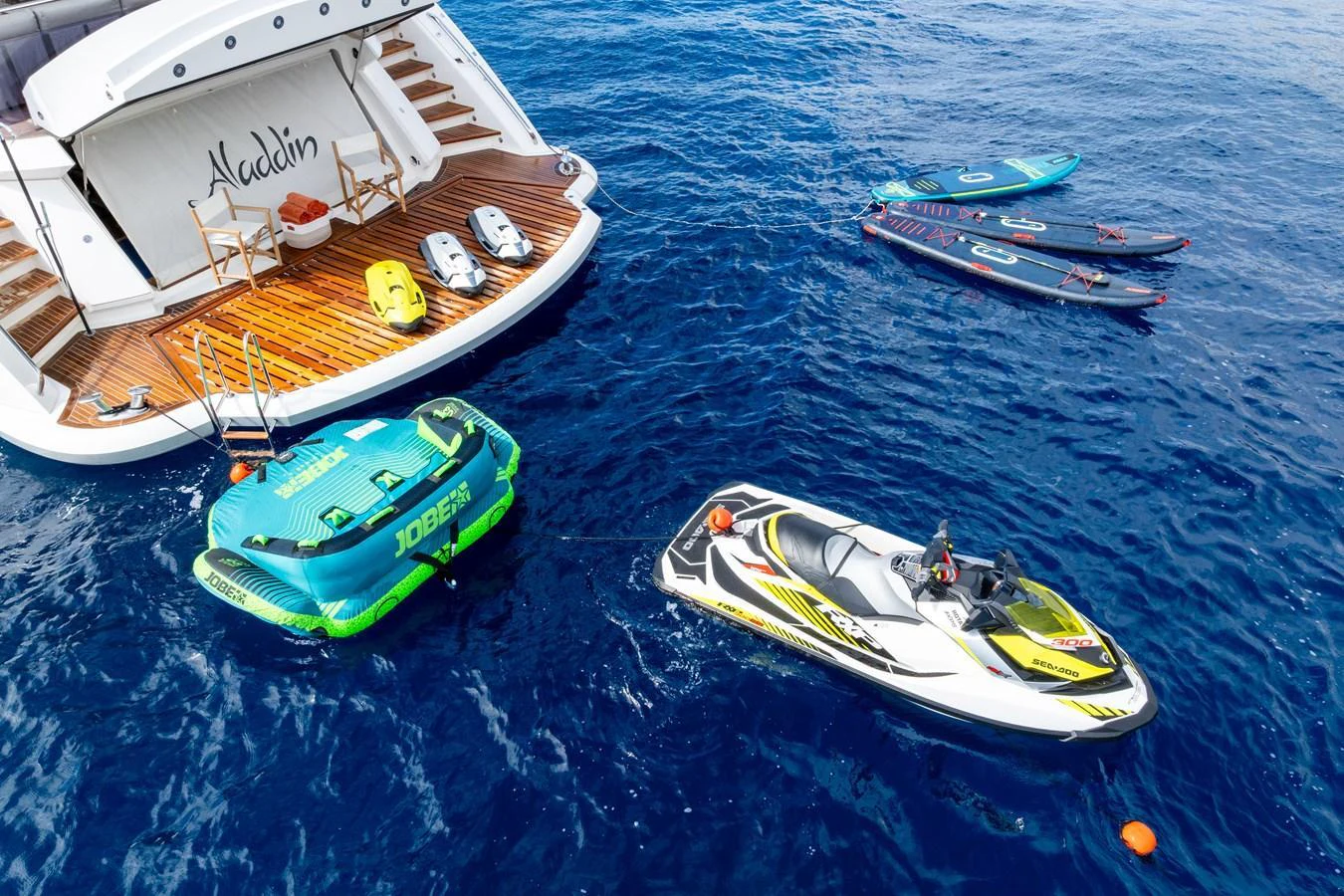 A luxurious yacht is accompanied by various water toys and tenders in a serene blue sea. aboard ALADDIN Yacht for Sale