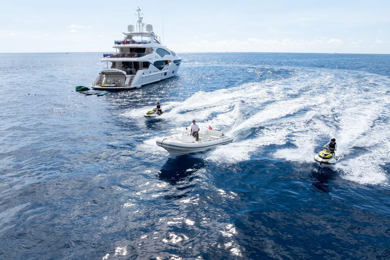 A luxurious yacht is anchored in the open sea, accompanied by a tender and jet skis creating an adventurous atmosphere. aboard ALADDIN Yacht for Sale