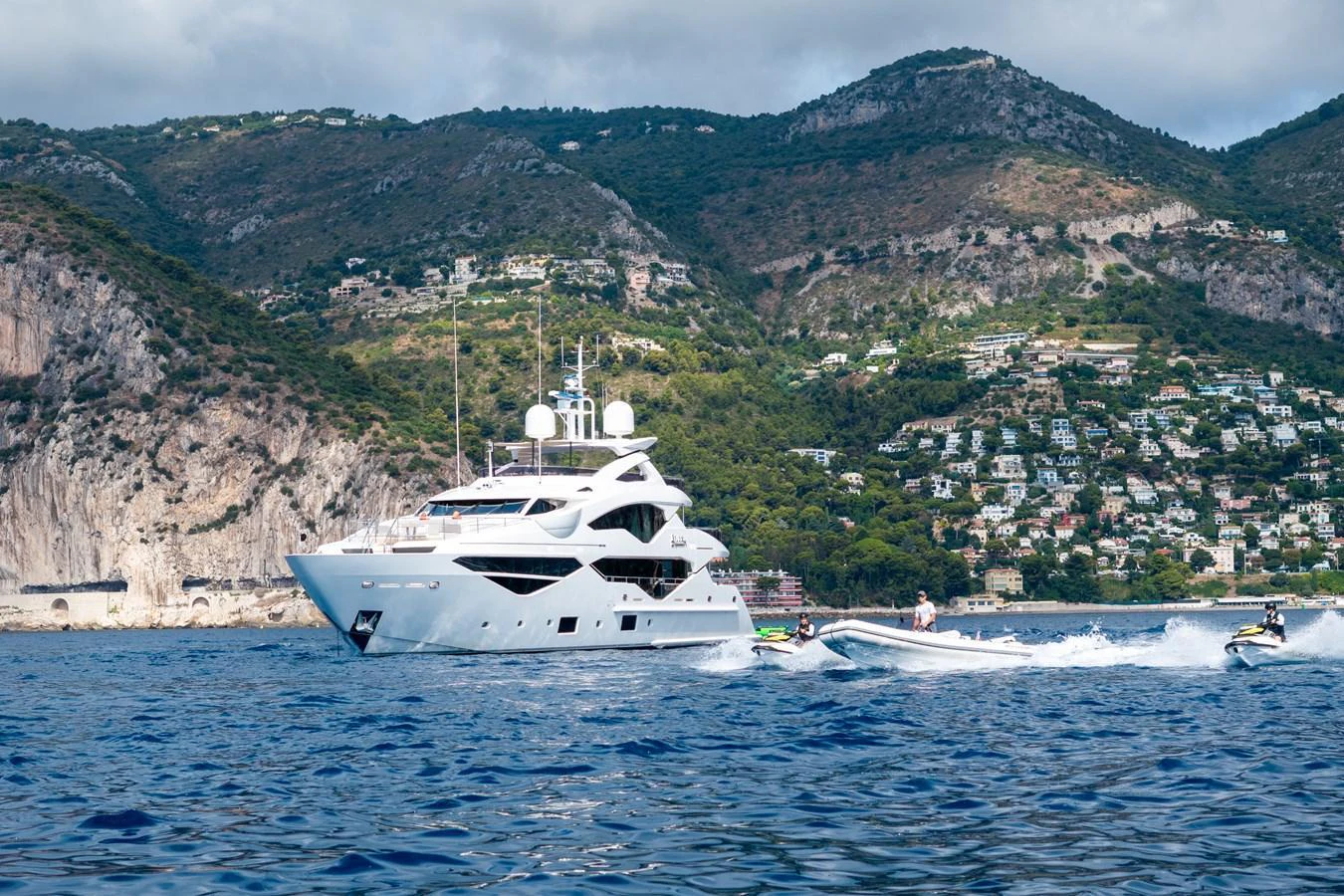 A luxurious yacht cruises along a scenic coastline with hills and houses in the background. aboard ALADDIN Yacht for Sale