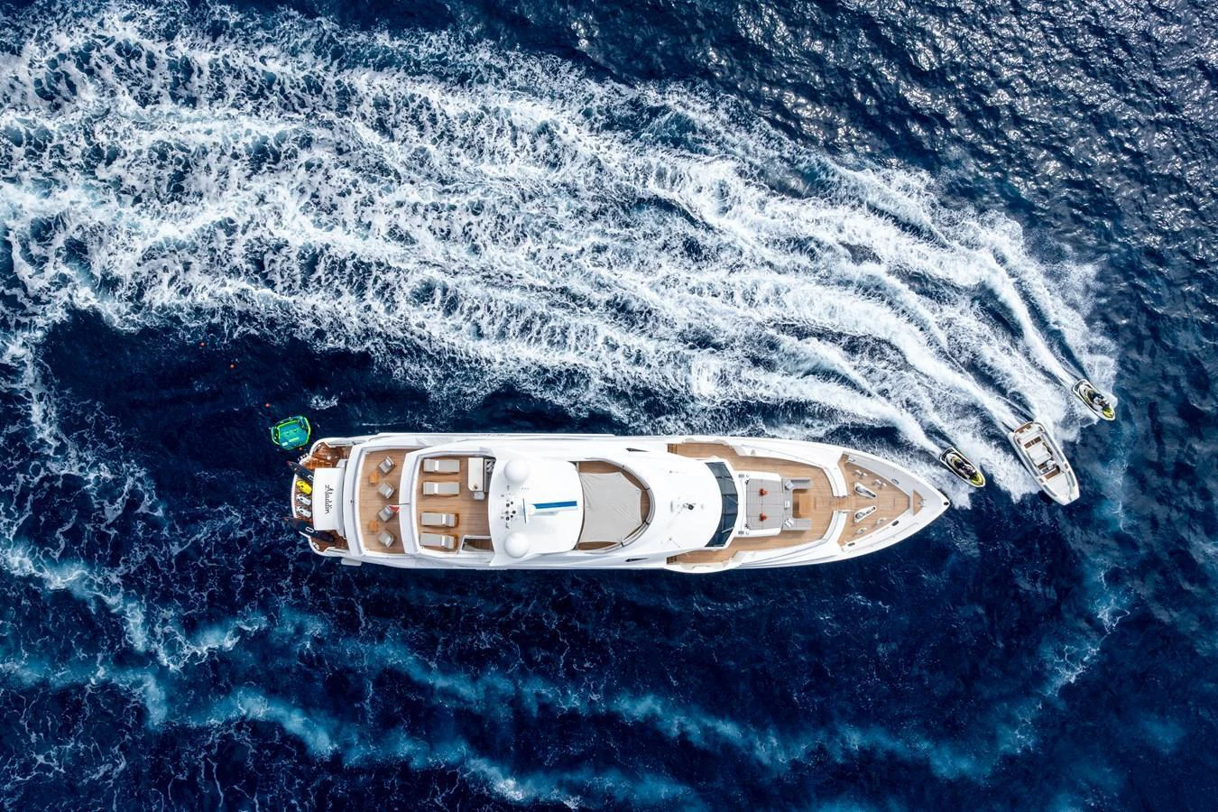A stunning aerial view of a luxurious yacht cruising through the open sea, accompanied by two smaller boats. aboard ALADDIN Yacht for Sale