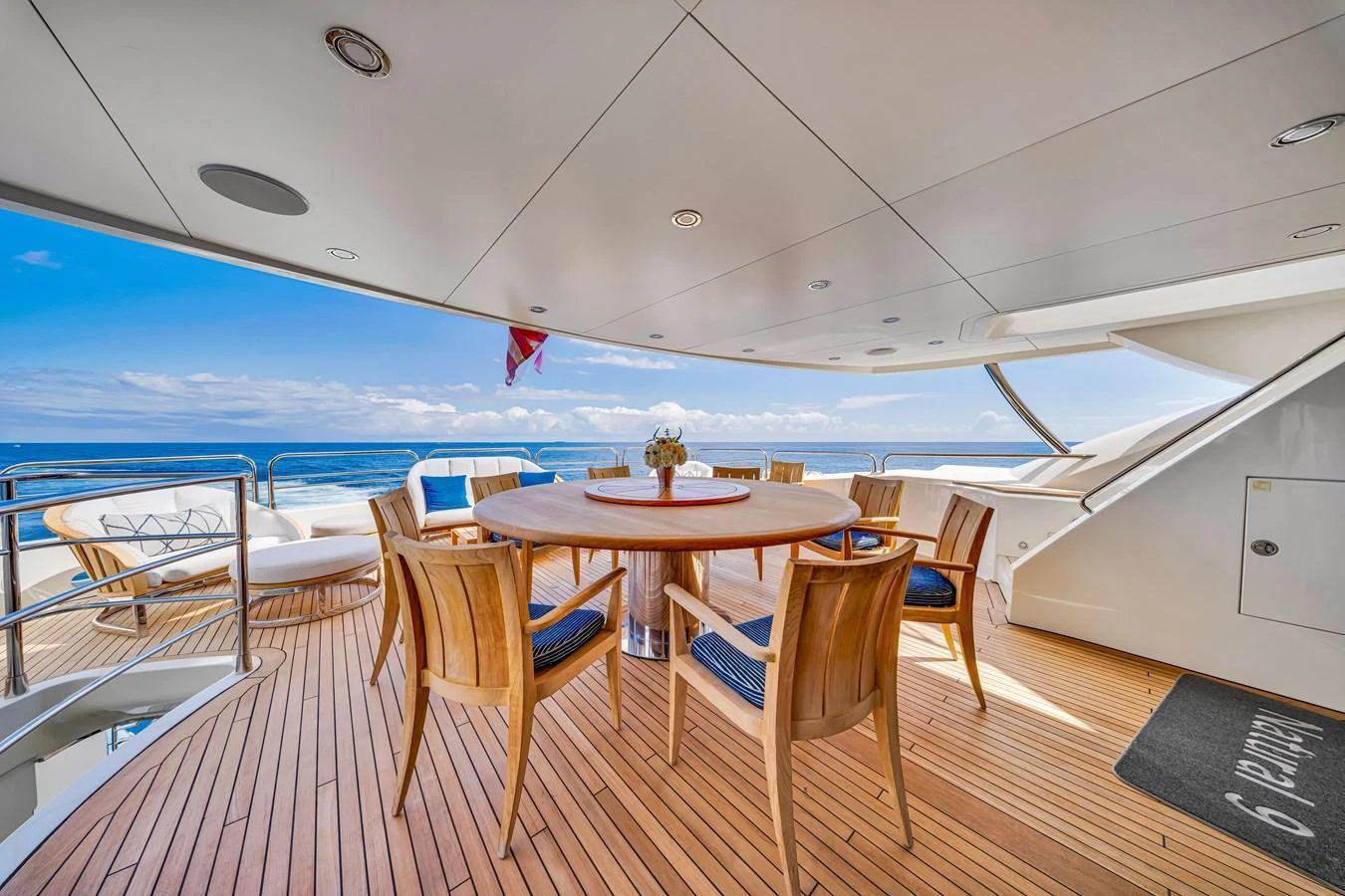 The aft deck features an elegant dining area with a round table and wooden chairs, offering stunning ocean views. aboard NATURAL 9 Yacht for Sale