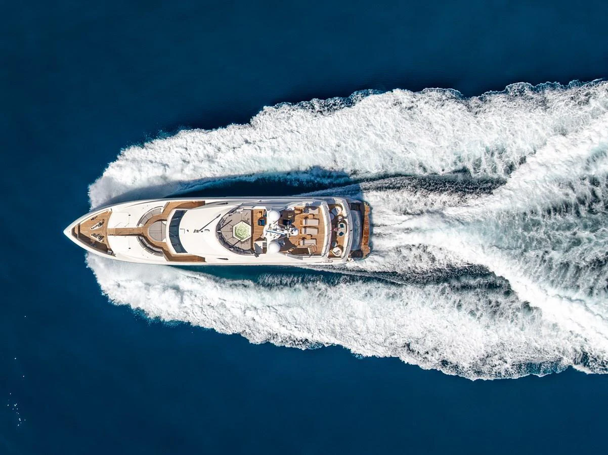 An aerial view of a luxurious yacht cruising through the deep blue sea, leaving a trail of white waves behind. aboard NATURAL 9 Yacht for Sale