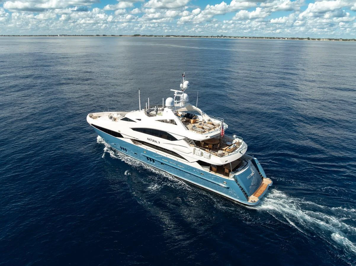 A luxurious yacht cruises through calm, deep blue waters under a partly cloudy sky. aboard NATURAL 9 Yacht for Sale