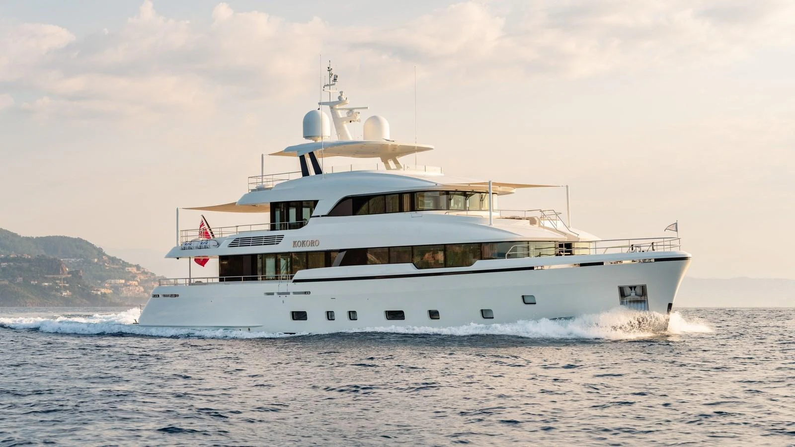 A luxurious yacht cruising on calm waters with scenic coastal views in the background. aboard KOKORO Yacht for Sale
