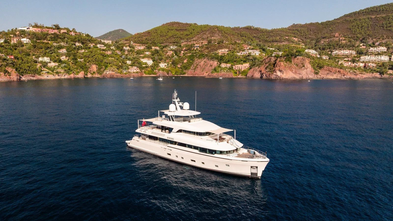 A stunning yacht glides gracefully on calm waters with a picturesque coastal backdrop. aboard KOKORO Yacht for Sale