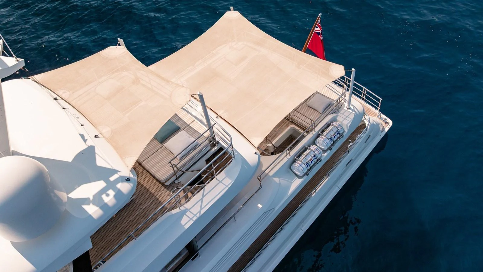 The yacht features a spacious sundeck with shaded lounging areas and a flag at the stern. aboard KOKORO Yacht for Sale