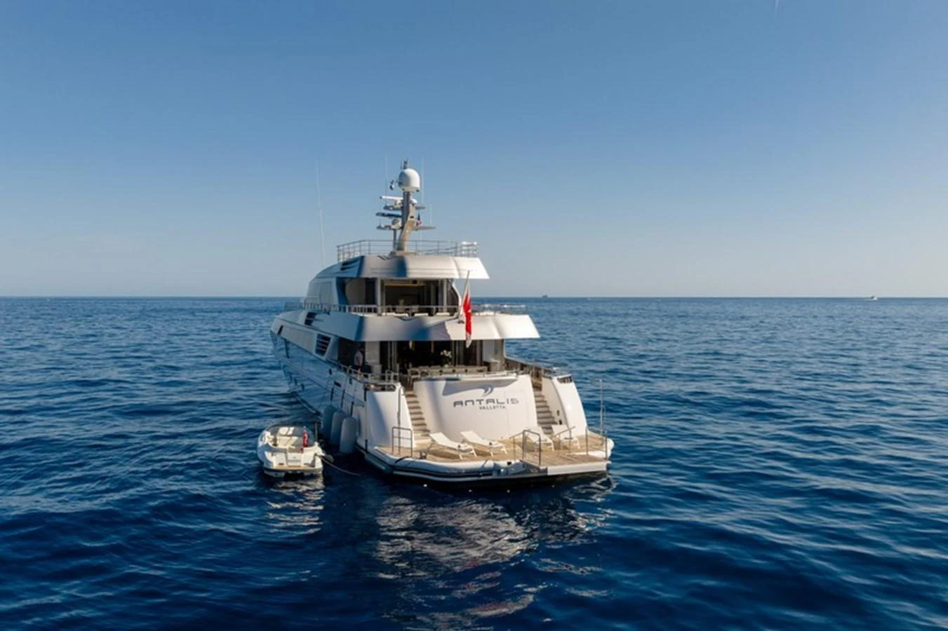 The yacht is seen from the rear, showcasing its expansive aft deck and tender on a calm sea. aboard ANTALIS Yacht for Sale