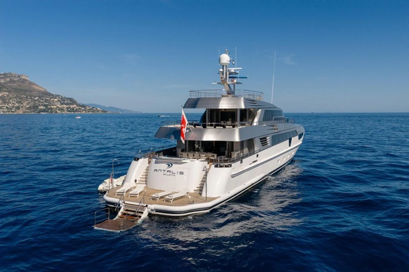 A luxurious yacht is anchored in calm blue waters with a scenic coastline in the background. aboard ANTALIS Yacht for Sale