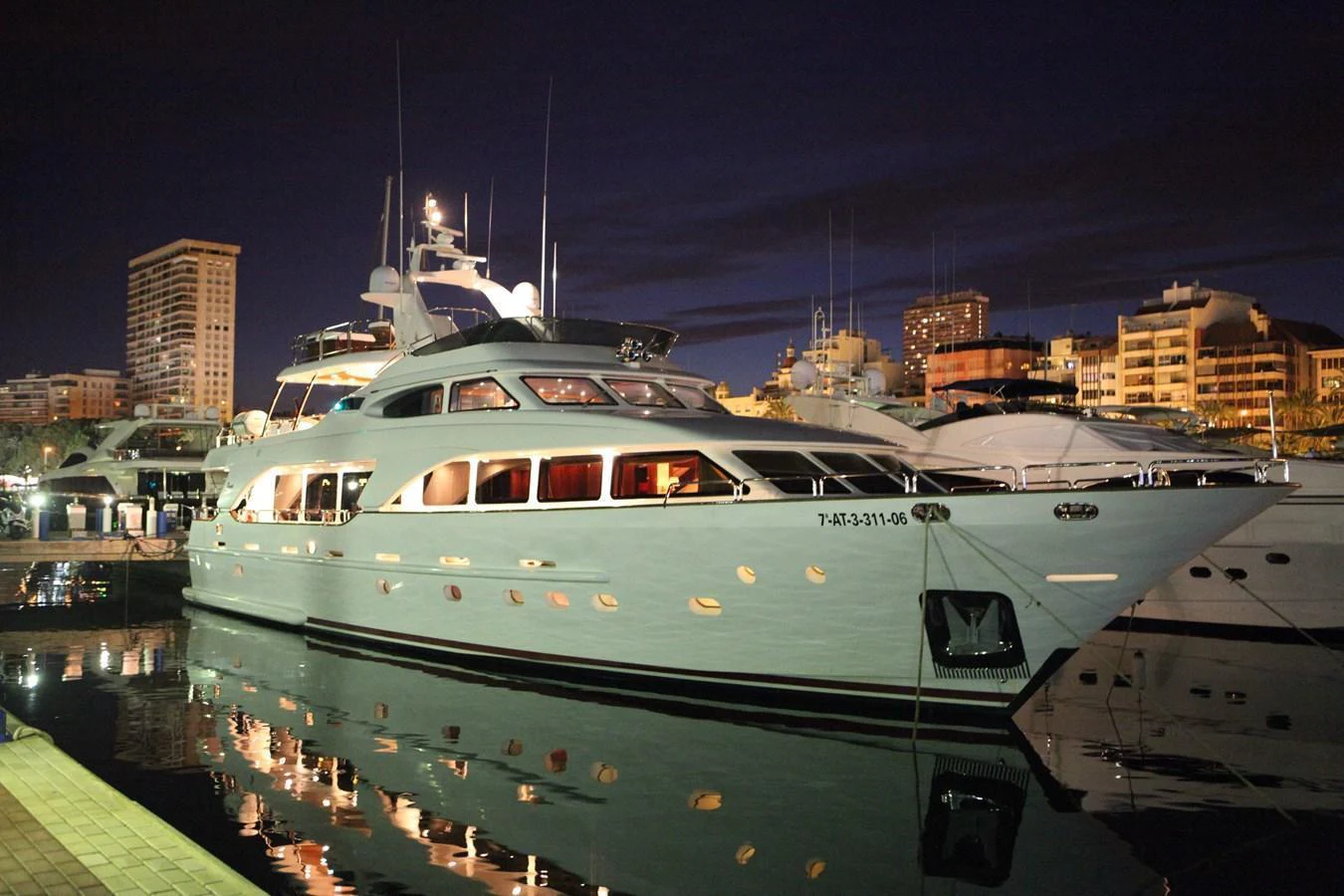 A luxurious yacht is docked at a marina under the night sky, reflecting beautifully on the calm water. aboard ANYPA Yacht for Sale