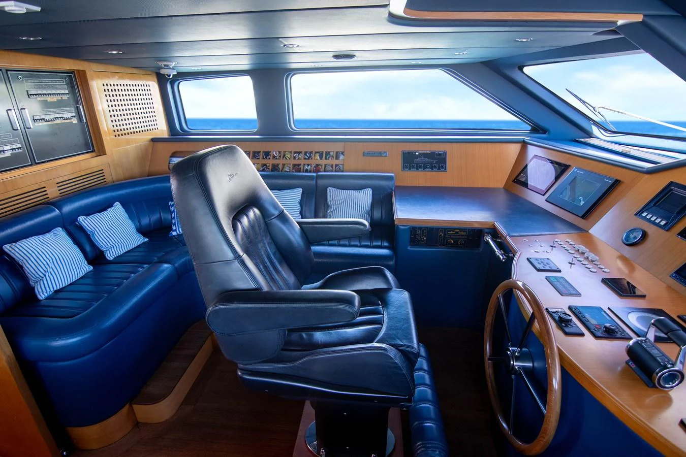 The helm station features a luxurious captain's chair and advanced navigation equipment, surrounded by rich wood paneling and plush seating. aboard ANYPA Yacht for Sale