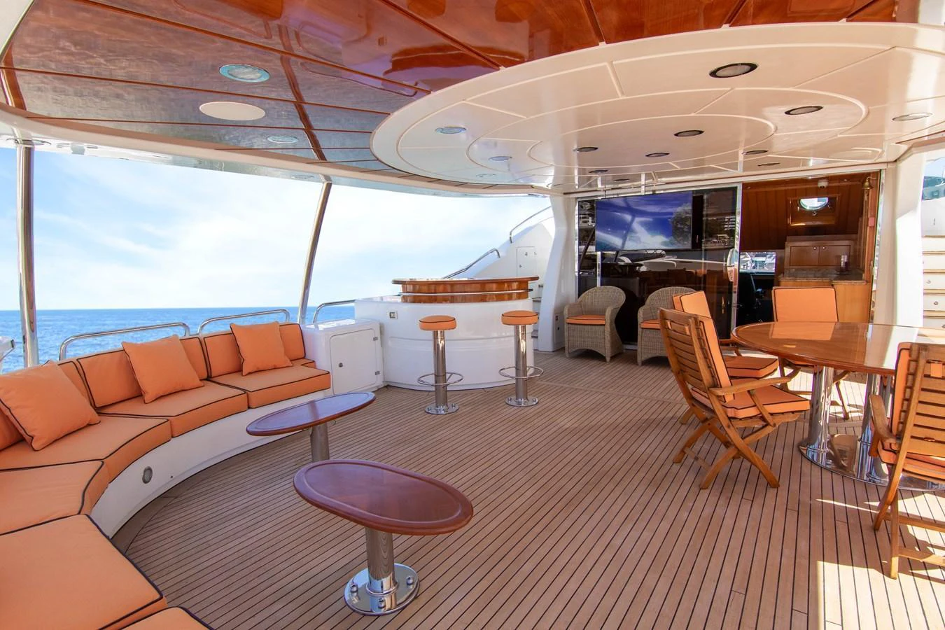The aft deck features a spacious seating area with plush cushions, a bar, and a dining table, all under a polished wooden ceiling. aboard ANYPA Yacht for Sale