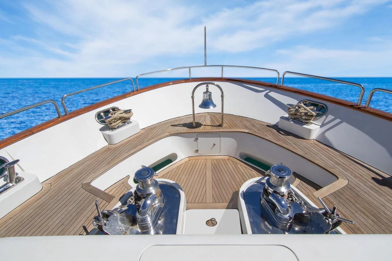 The foredeck features polished winches and a bell, set against a backdrop of clear blue skies and sea. aboard ANYPA Yacht for Sale