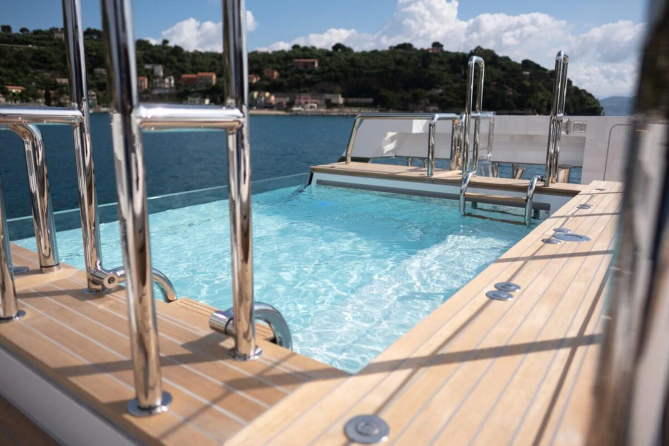 The yacht features a luxurious pool with gleaming stainless steel railings and a stunning view of the coastline. aboard TOLEMAI Yacht for Sale