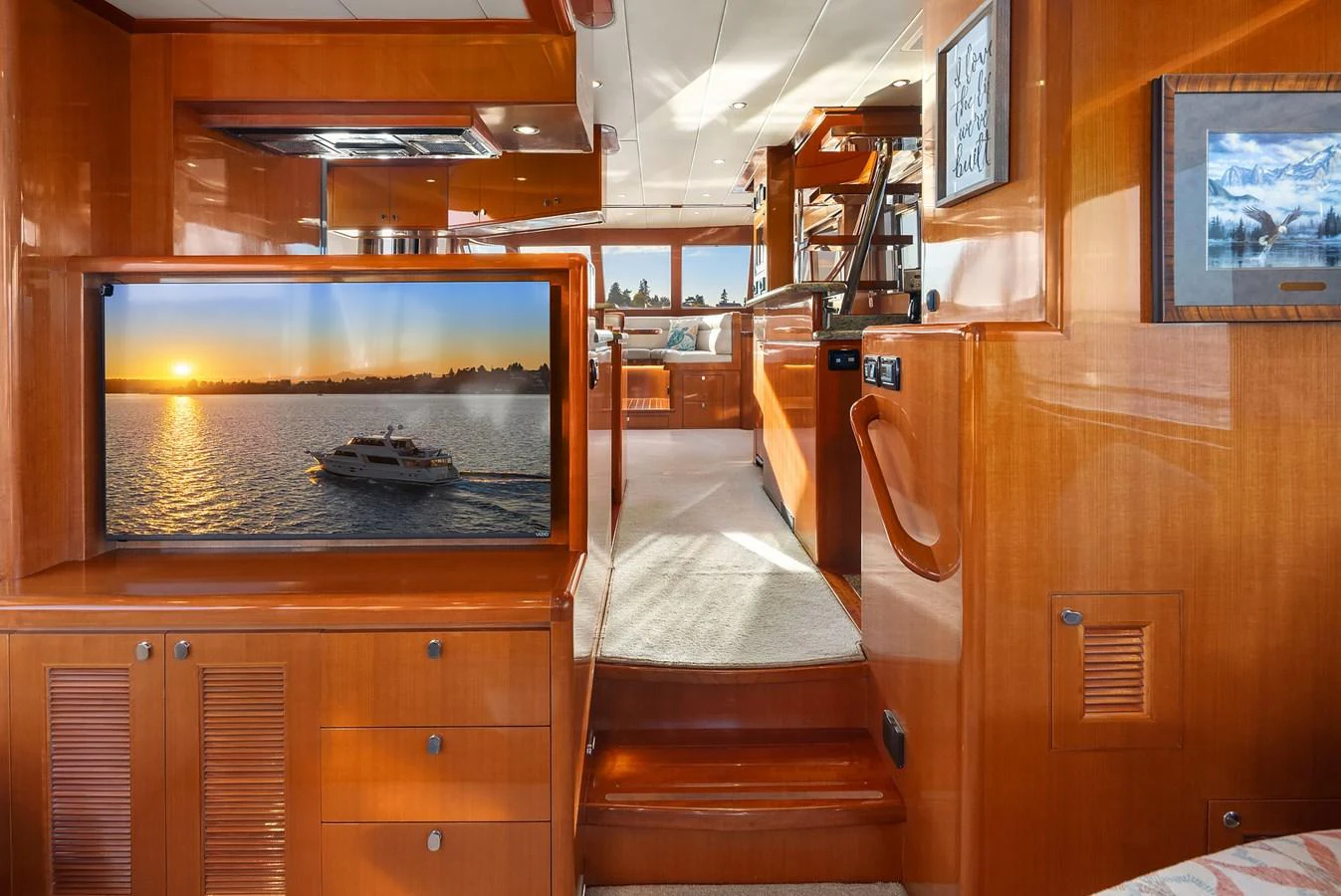 The salon features warm wood finishes and a flat-screen TV displaying a serene sunset scene. aboard LA BELLA VITA II Yacht for Sale