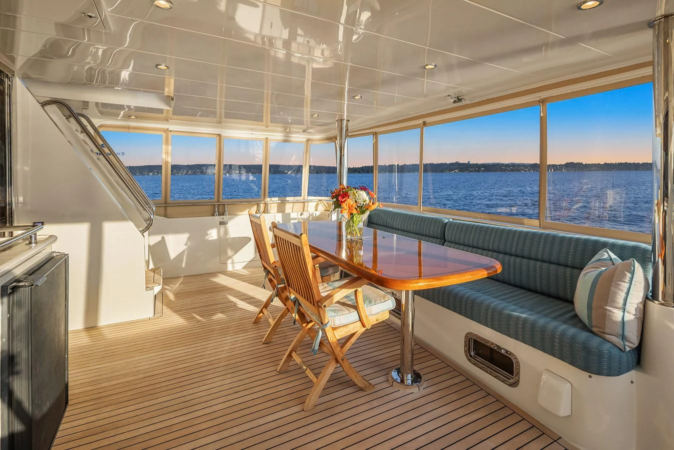 The aft deck features a spacious seating area with a wooden table and chairs, offering stunning views of the water. aboard LA BELLA VITA II Yacht for Sale