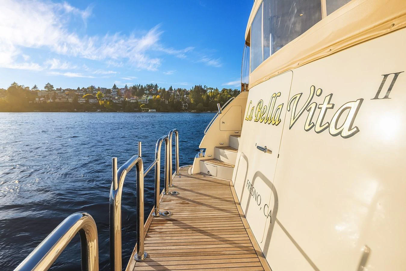 A serene view of the yacht's side deck with a backdrop of calm waters and a distant shoreline. aboard LA BELLA VITA II Yacht for Sale