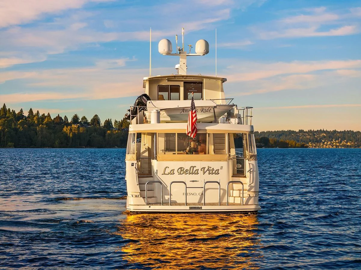 A luxurious yacht is seen from the rear, cruising on calm waters with a scenic backdrop. aboard LA BELLA VITA II Yacht for Sale