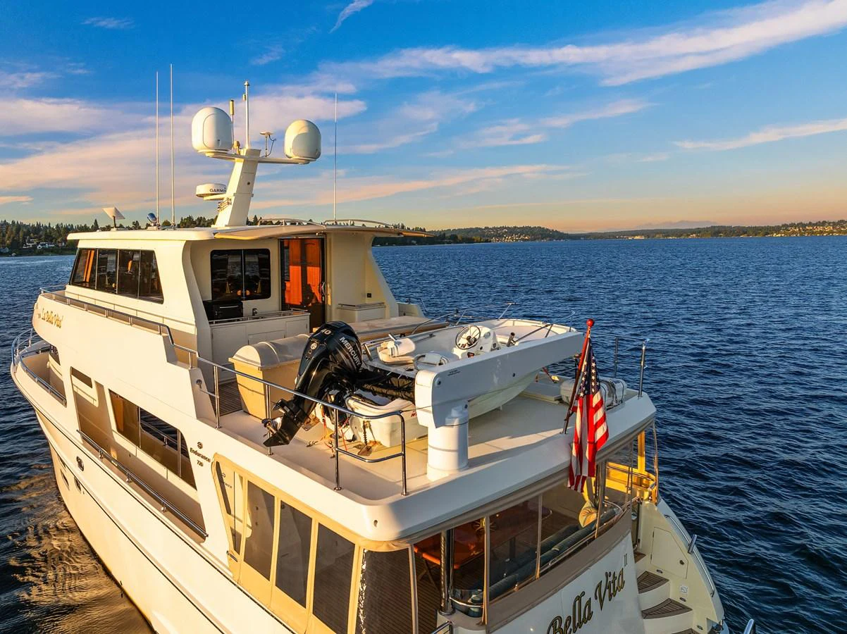 The yacht is anchored on calm waters with a clear view of the aft deck and surrounding scenery. aboard LA BELLA VITA II Yacht for Sale