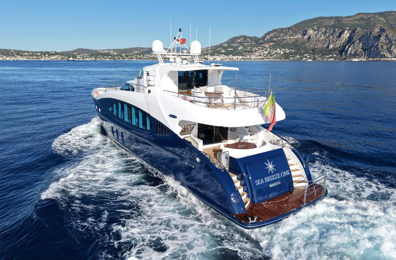 A luxurious yacht cruises through clear blue waters with scenic coastal mountains in the background. aboard SEA BREEZE ONE Yacht for Sale