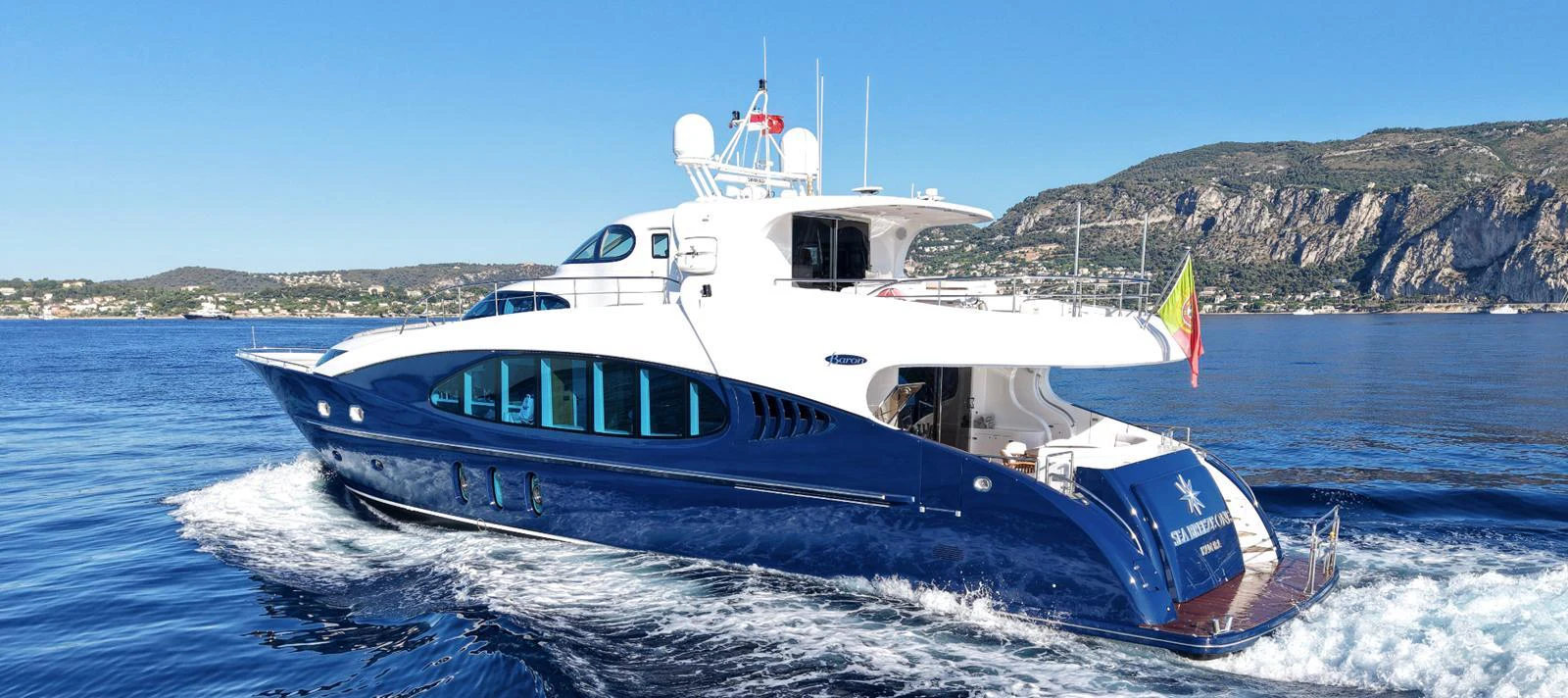 A sleek yacht cruises through clear blue waters with a scenic coastline in the background. aboard SEA BREEZE ONE Yacht for Sale