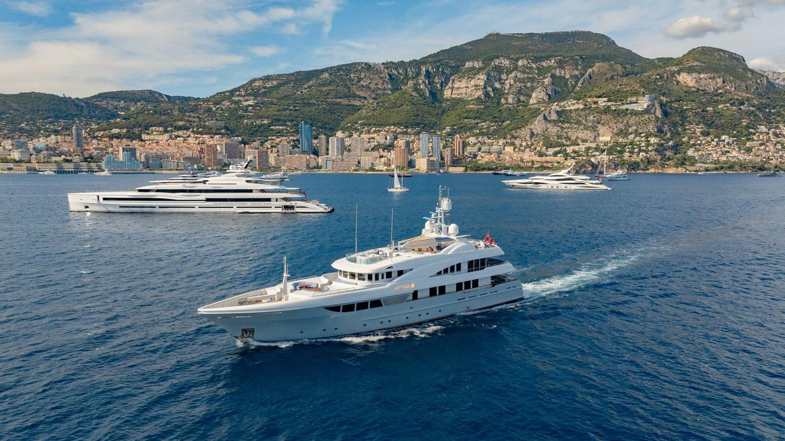 A luxurious yacht cruises through serene blue waters with a picturesque coastal backdrop. aboard LATITUDE Yacht for Sale