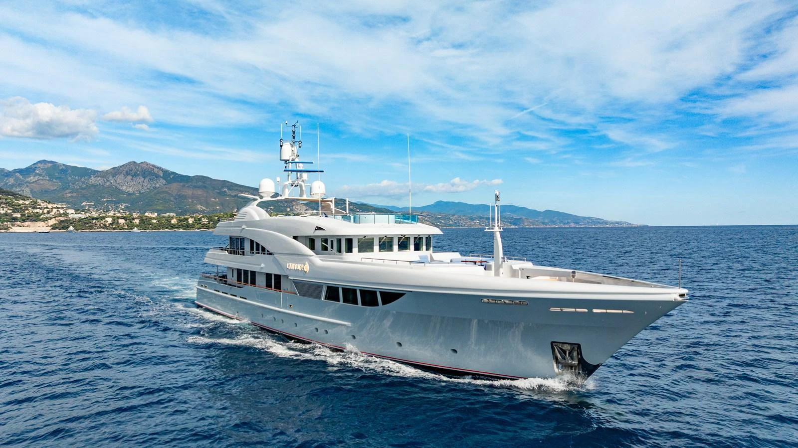 A luxurious yacht cruises through serene blue waters with a stunning coastal backdrop. aboard LATITUDE Yacht for Sale