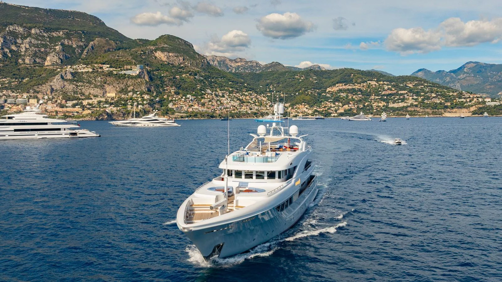 A luxurious yacht cruises through serene blue waters with a picturesque coastal backdrop. aboard LATITUDE Yacht for Sale