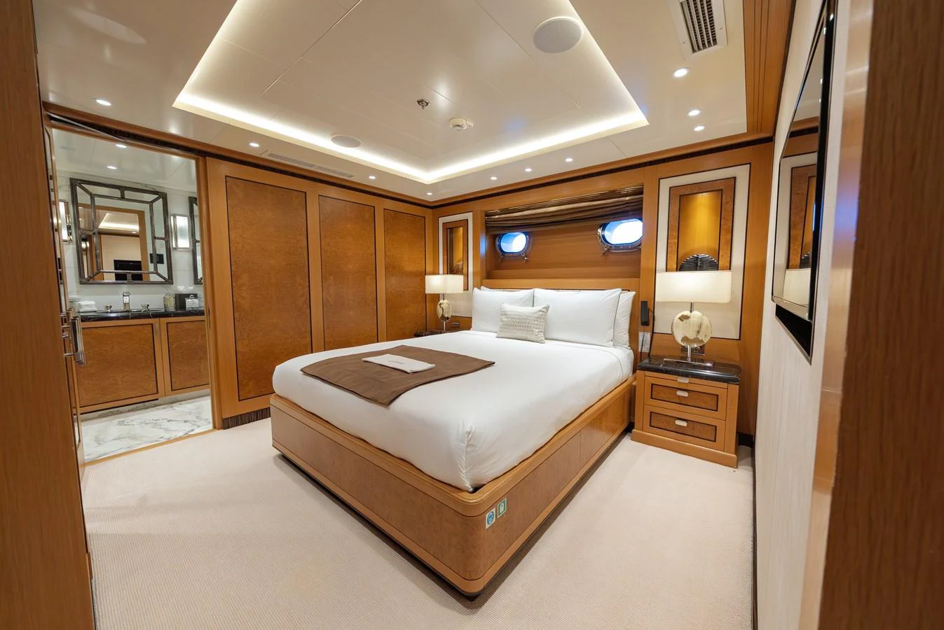 The master stateroom features a luxurious bed with elegant wooden finishes and ambient lighting. aboard LATITUDE Yacht for Sale