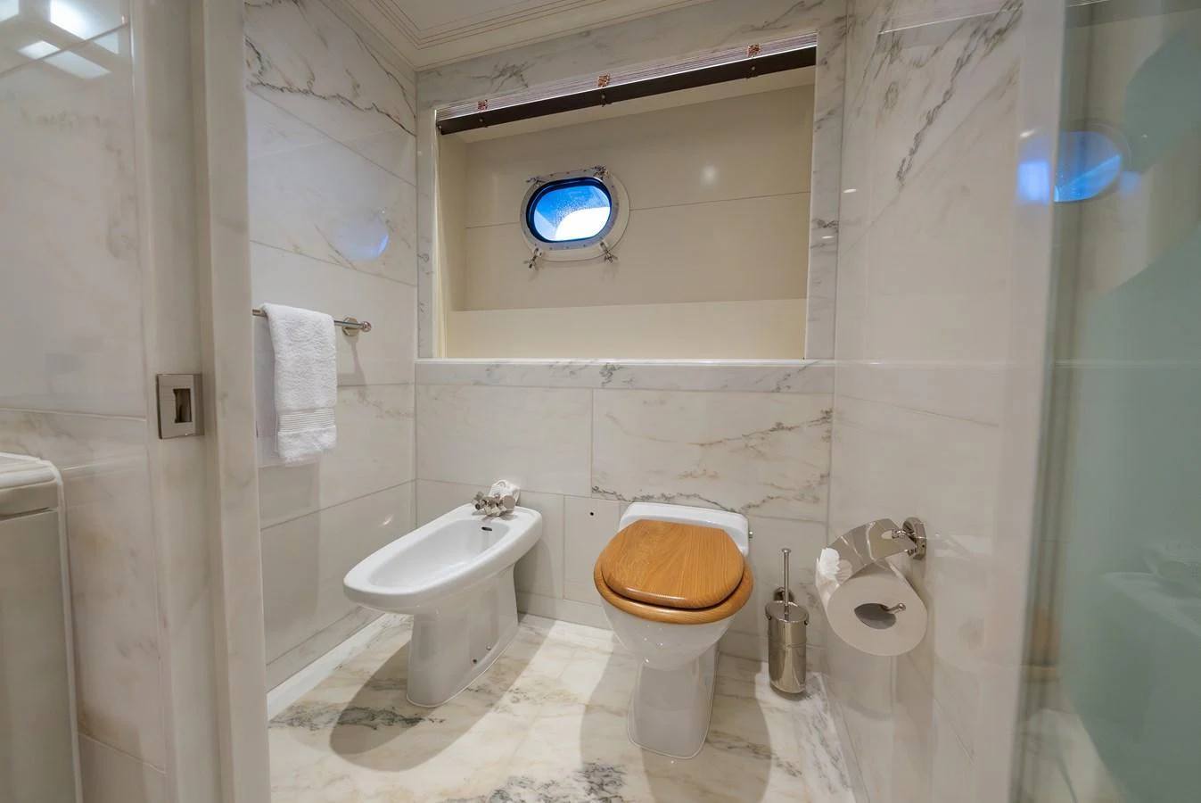 The bathroom features elegant marble surfaces and a porthole window for natural light. aboard LATITUDE Yacht for Sale