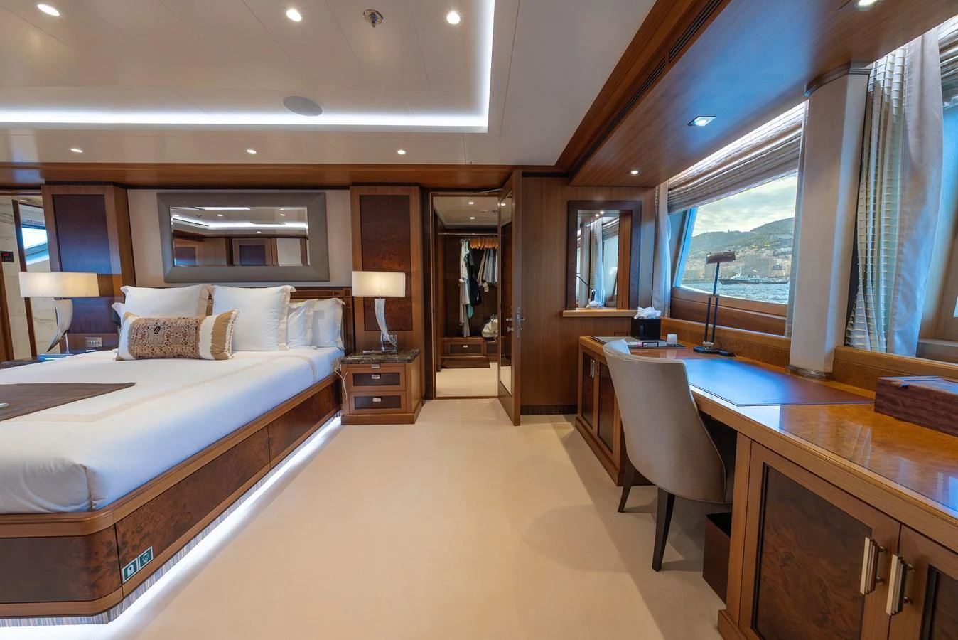 The master stateroom features luxurious wood finishes, a spacious bed, and a well-appointed desk area with large windows offering scenic views. aboard LATITUDE Yacht for Sale