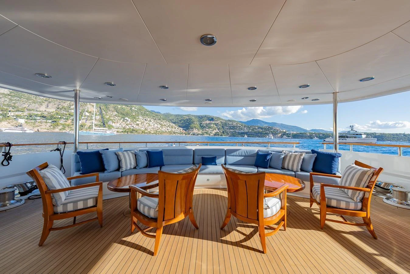 The aft deck features a spacious seating area with wooden chairs and tables, offering stunning views of the surrounding waters. aboard LATITUDE Yacht for Sale