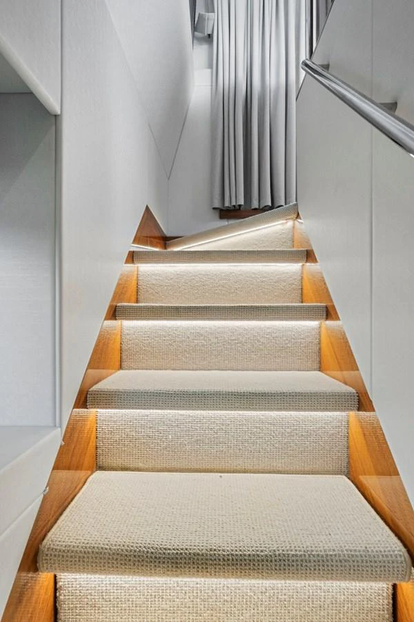 A modern staircase with soft lighting and elegant carpeting leads to the upper deck. aboard EXIT Yacht for Sale
