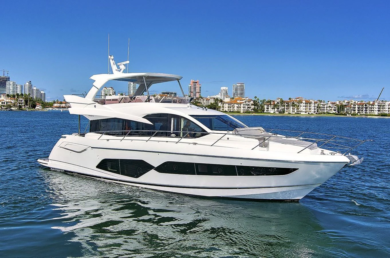 A sleek and modern yacht cruising on calm waters with a cityscape in the background. aboard EXIT Yacht for Sale