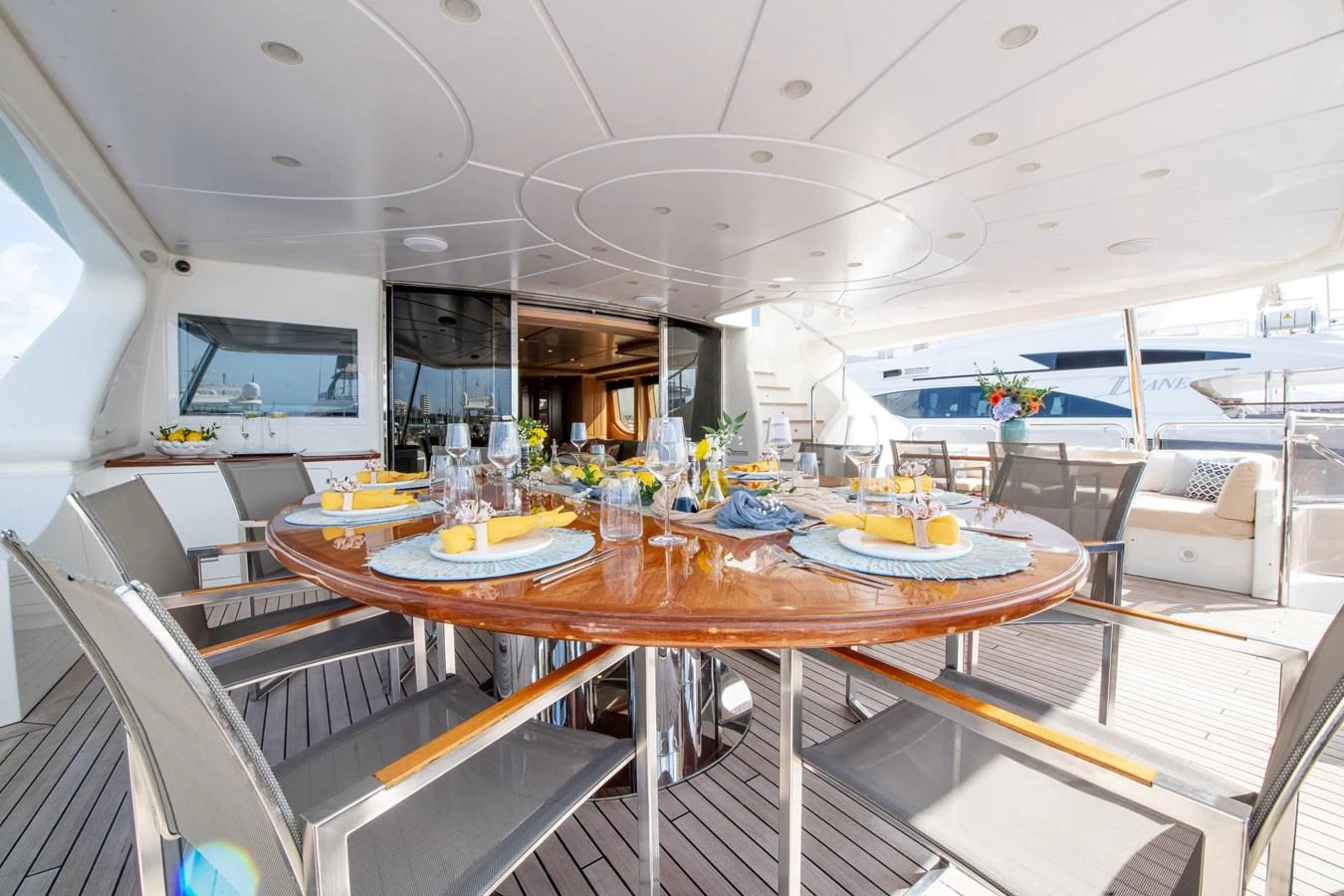 The aft deck features an elegant dining area with a large round table set for a meal, offering a perfect spot for alfresco dining. aboard SOHO Yacht for Sale