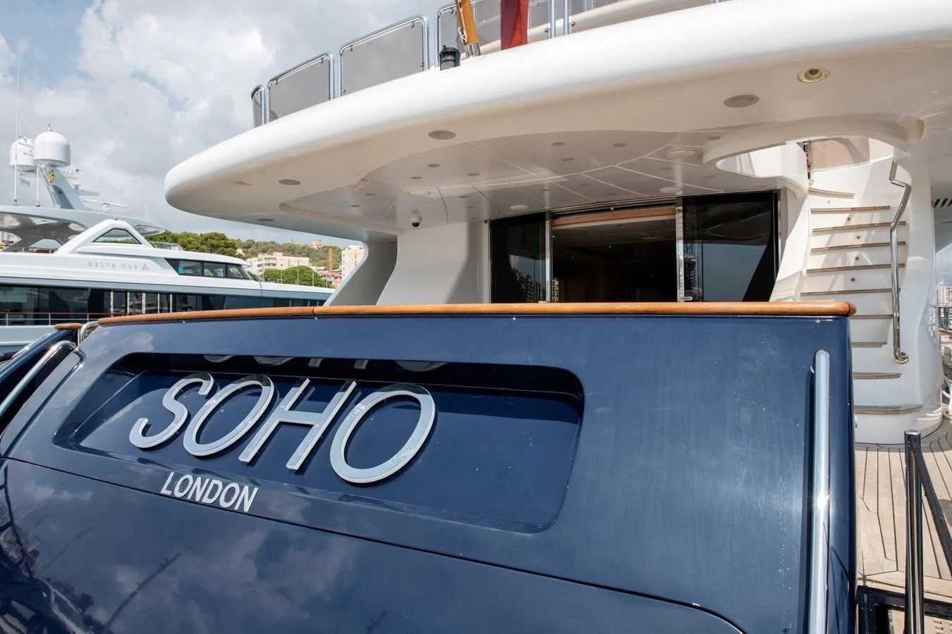 The image showcases the stern of a yacht docked at a marina, highlighting its name and elegant design. aboard SOHO Yacht for Sale