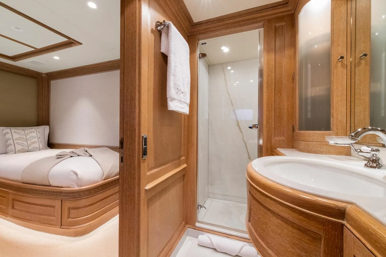 The guest stateroom features a cozy bed and an en-suite bathroom with elegant wooden finishes. aboard SOHO Yacht for Sale