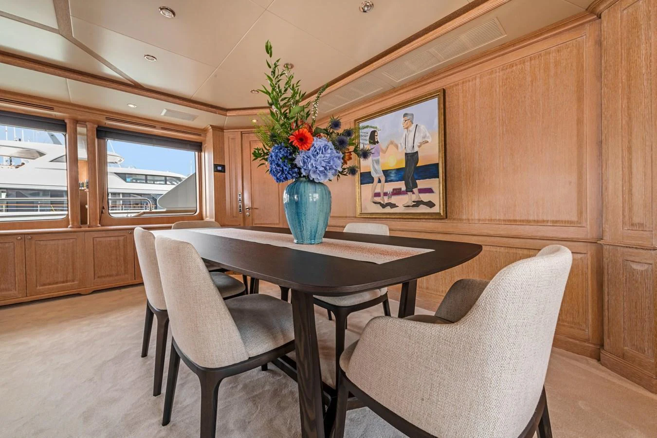 The yacht's dining area features a sophisticated setting with a stylish table and comfortable chairs, complemented by a beautiful floral arrangement. aboard SOHO Yacht for Sale