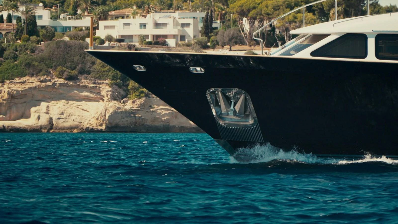 The sleek bow of a yacht cuts through the water near a scenic coastline. aboard SOHO Yacht for Sale