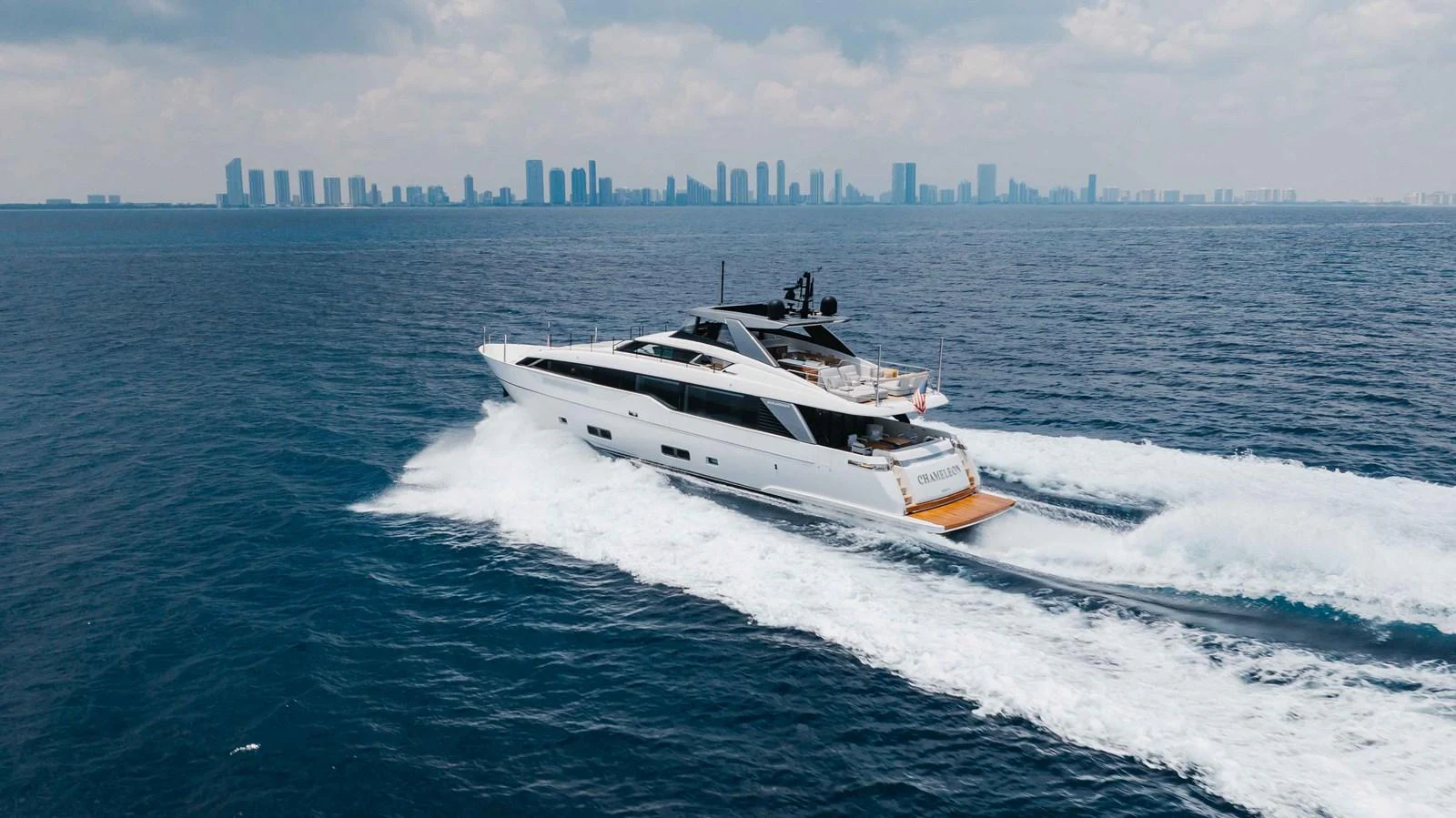 A sleek yacht cruises through the open water with a city skyline in the background. aboard CHAMELEON Yacht for Sale