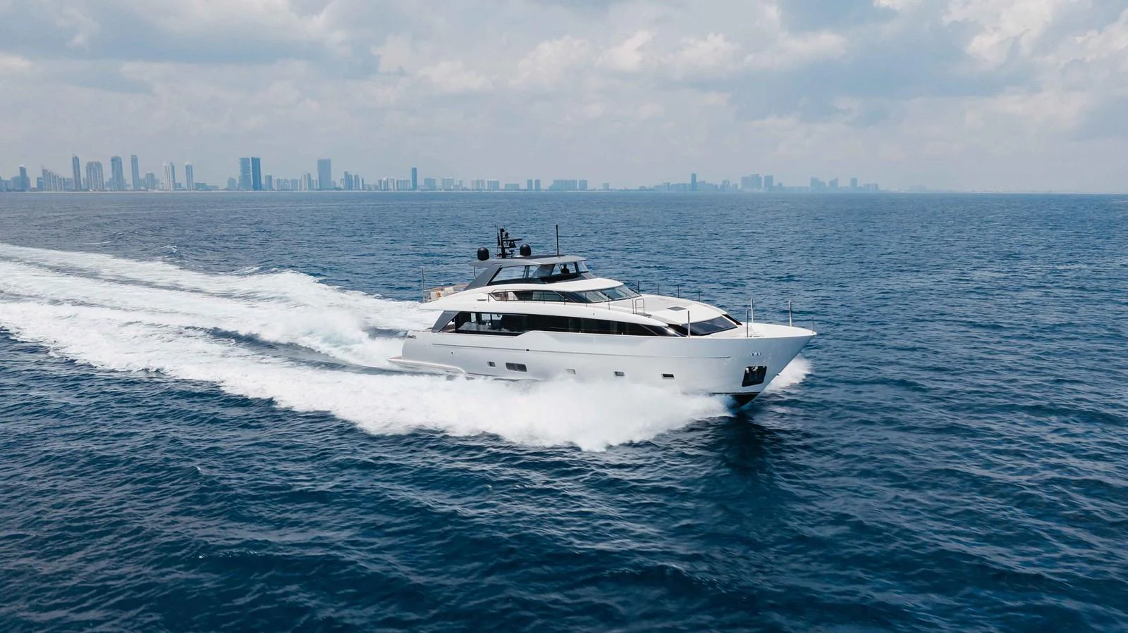 A sleek yacht cruises swiftly on open waters with a city skyline in the background. aboard CHAMELEON Yacht for Sale