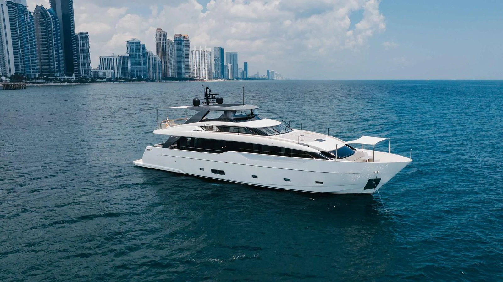 A sleek and modern yacht cruising near a city skyline on a sunny day. aboard CHAMELEON Yacht for Sale