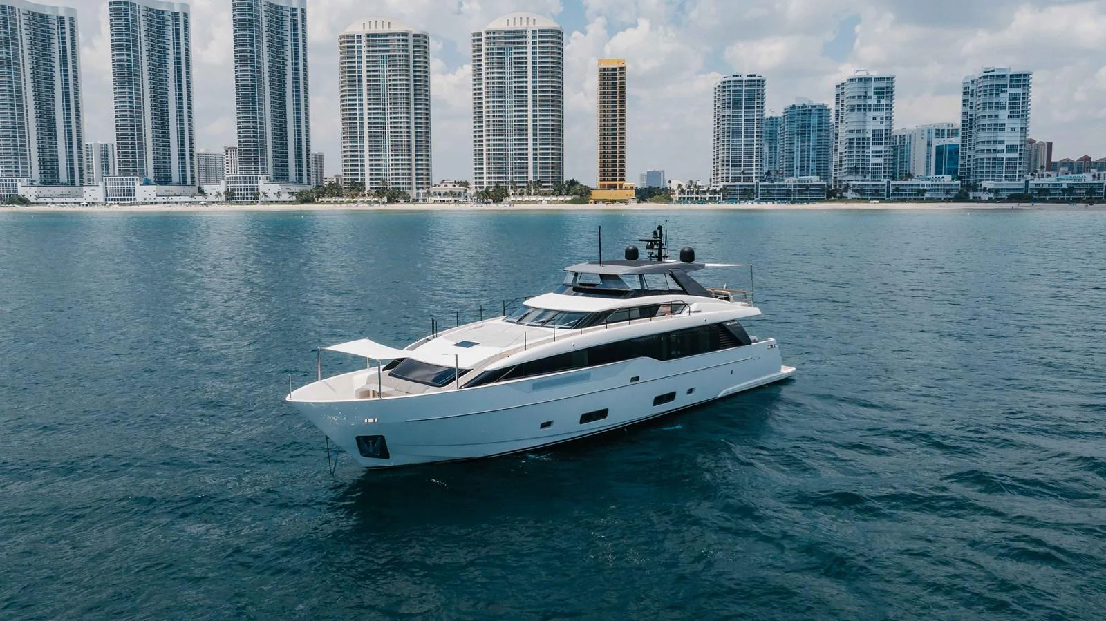 A sleek and modern yacht cruises gracefully on calm waters with a city skyline in the background. aboard CHAMELEON Yacht for Sale