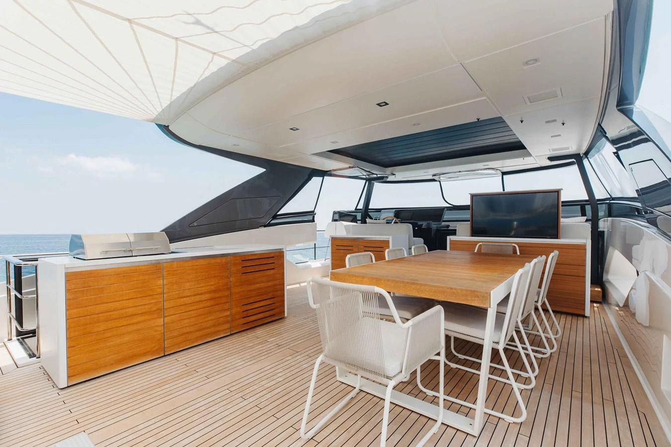 The aft deck features a spacious dining area with a wooden table and modern chairs, complemented by a built-in grill and ample storage. aboard CHAMELEON Yacht for Sale