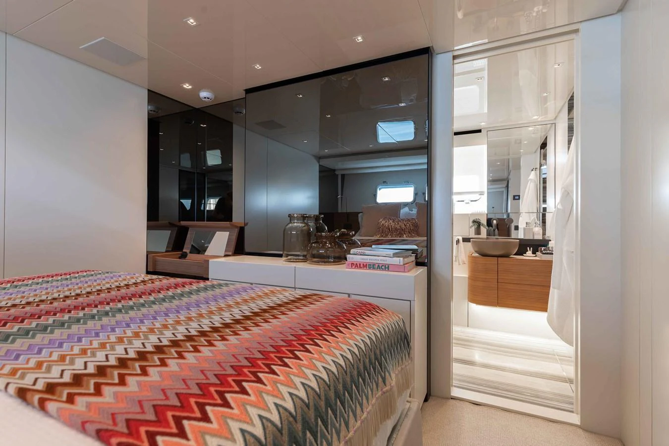 The stateroom features a cozy bed with a colorful patterned blanket and a view into the ensuite bathroom. aboard CHAMELEON Yacht for Sale