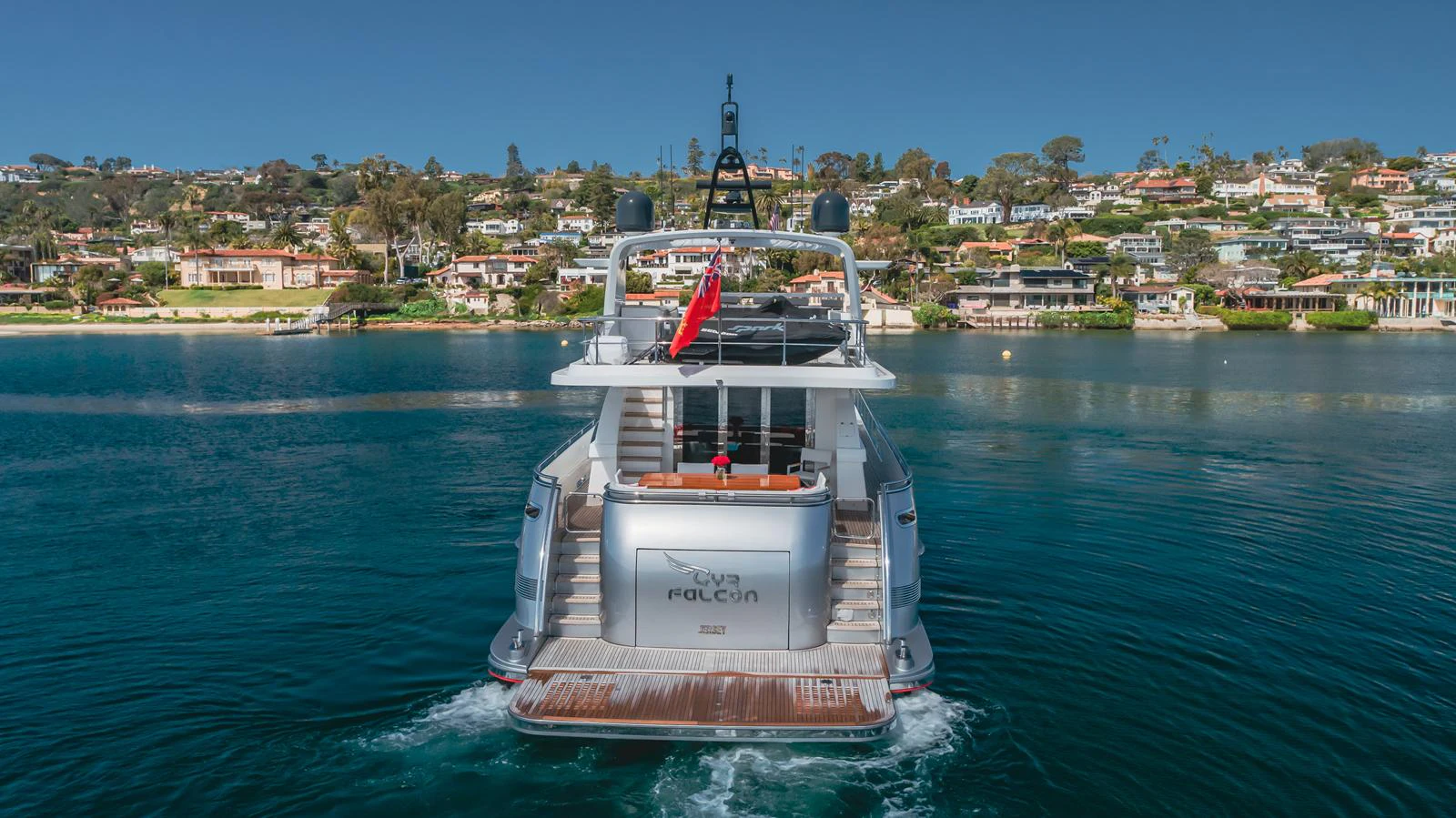 A sleek yacht is seen from the rear, cruising through calm waters with a scenic coastal backdrop. aboard TEST NAME Yacht for Sale