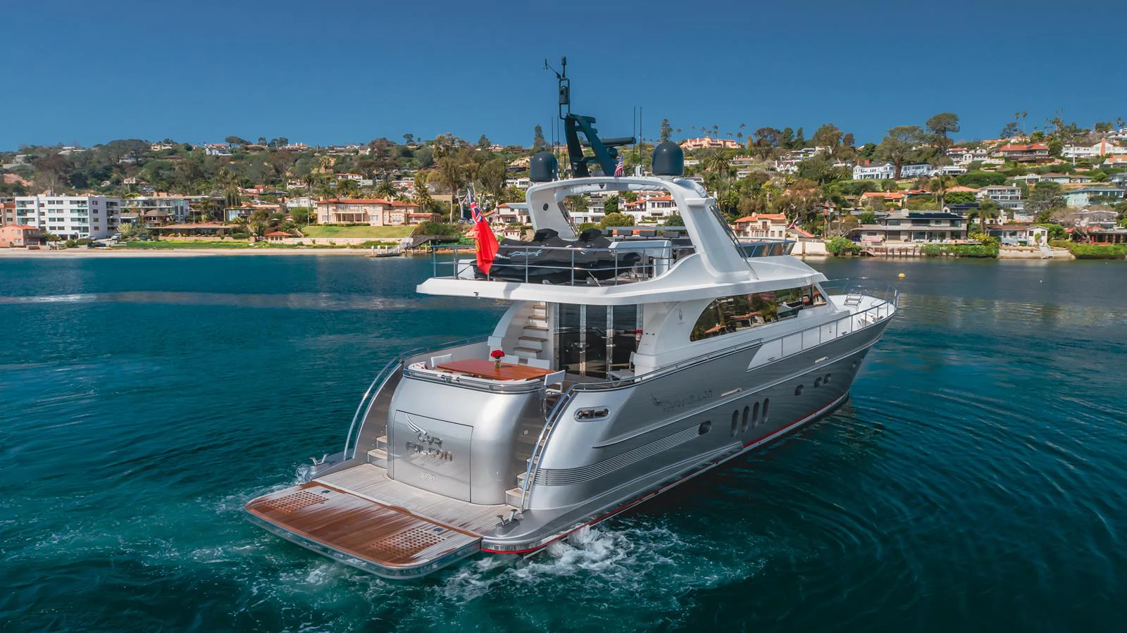 A sleek yacht cruises through calm waters with a scenic coastal backdrop. aboard TEST NAME Yacht for Sale