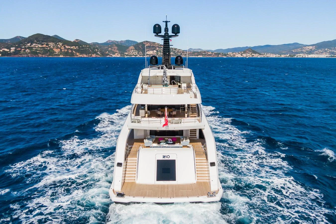 A luxurious yacht cruising through the open sea with a stunning coastal backdrop. aboard RIO Yacht for Sale