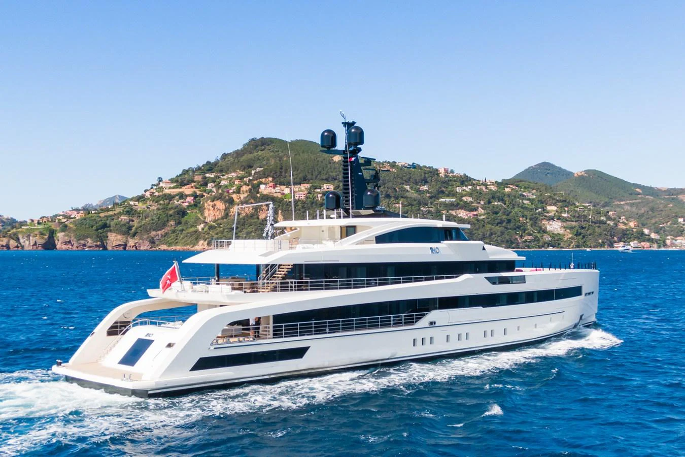 A sleek, modern yacht cruising on a clear blue sea with a scenic coastal backdrop. aboard RIO Yacht for Sale