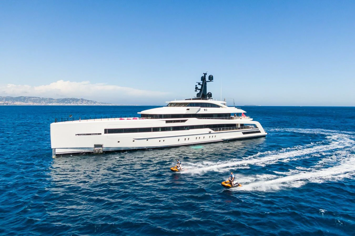 A sleek, modern yacht cruises through the open sea, accompanied by two jet skis. aboard RIO Yacht for Sale